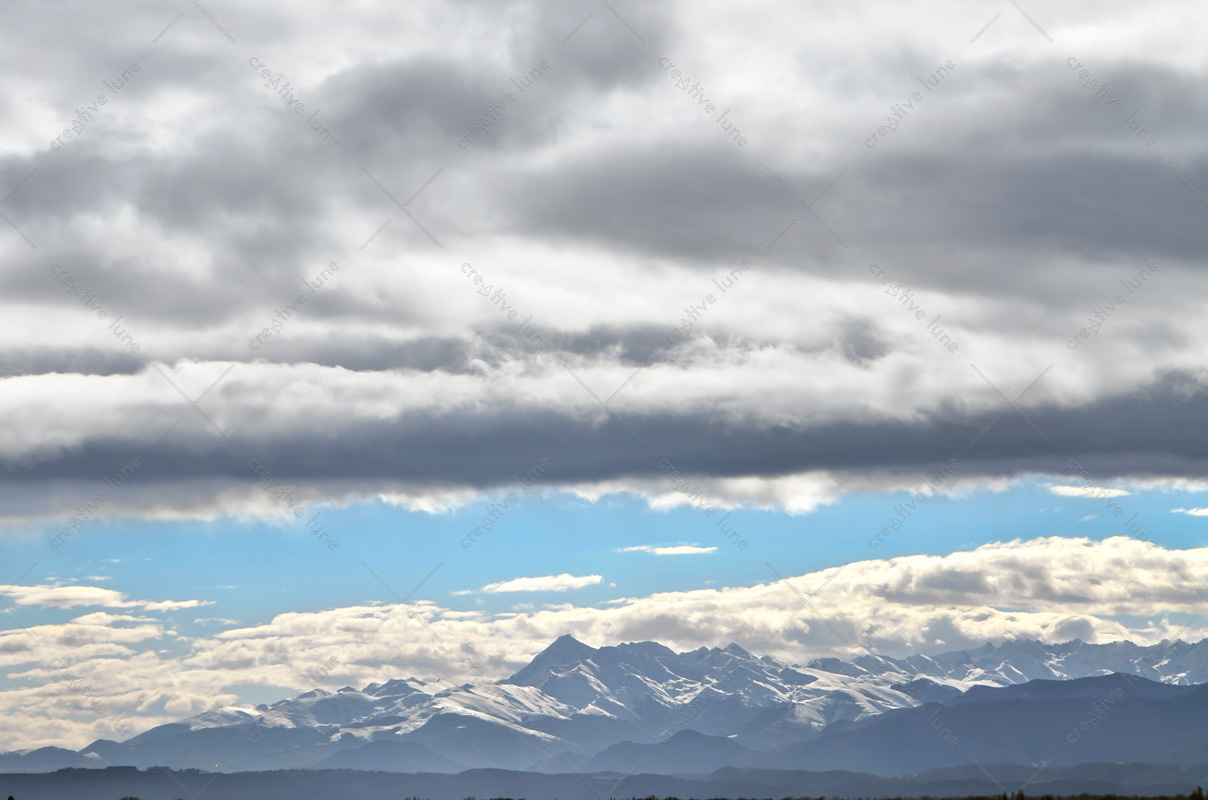 Nuages et Pyrénées bleues, photographie haute résolution d'un front nuageux parfaitement découpé devant la chaîne des Pyrénées blanchie par la neige.